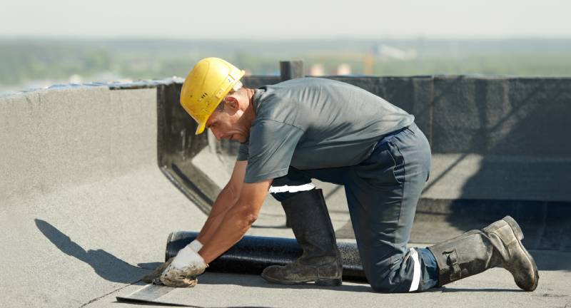 A man in yellow hard hat working on the roof of a building.